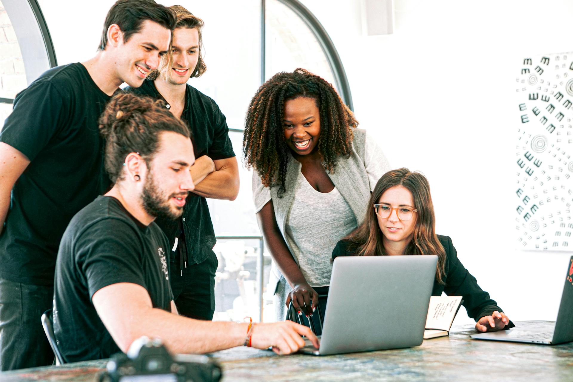 Group of five people standing around a laptop and smiling