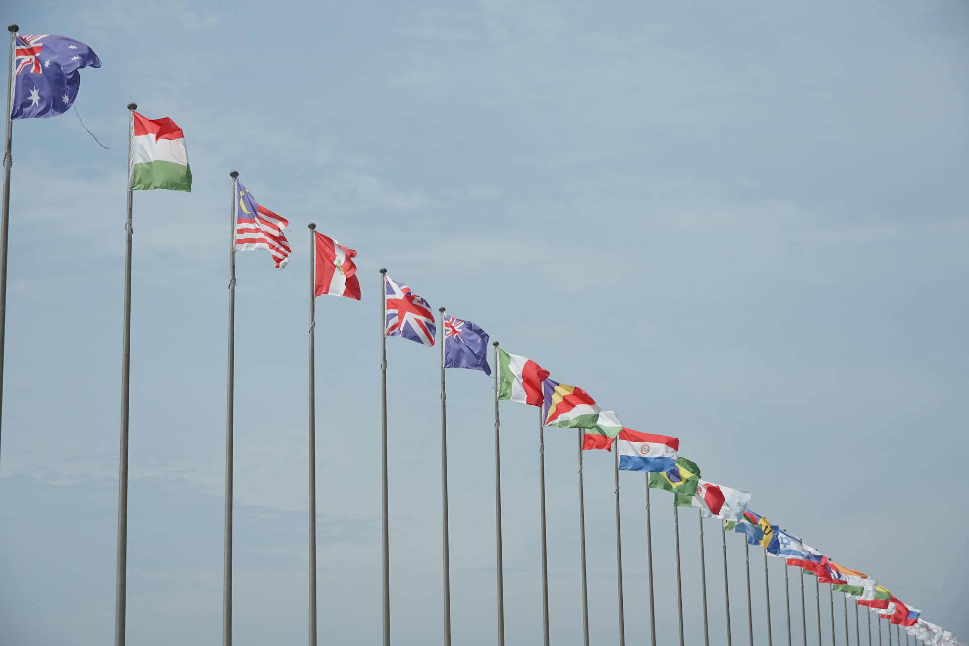 Twenty nine flags flying on flag poles in a line